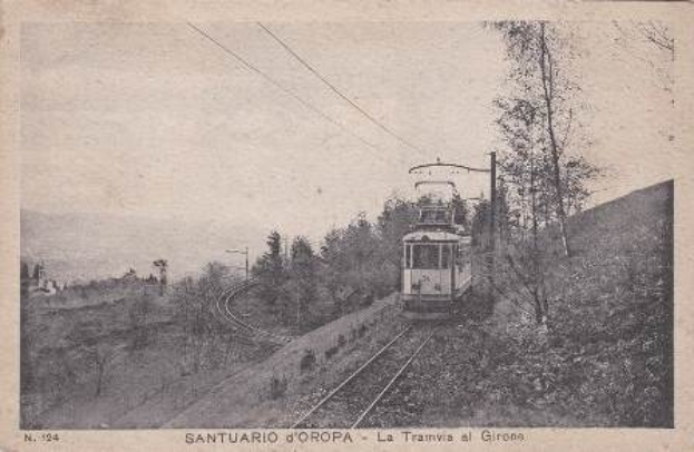 Schwarzes und weißes Foto eines Zuges auf Schienen umgeben von Bäumen, Pfählen und Oberleitungen mit Text unten.