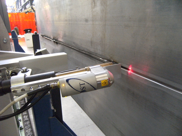 Hell leuchtender Laserstrahl aus einer Schneidmaschine in einer industriellen Fabrikumgebung mit einer Wand auf der rechten Seite und Hintergrundobjekten.