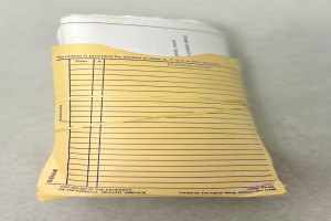 Ein Papierstapel mit einer gelben Schleife darum, der auf einem Tisch liegt, sieht aus wie eine medizinische Aufzeichnung mit darauf geschriebenem Text.