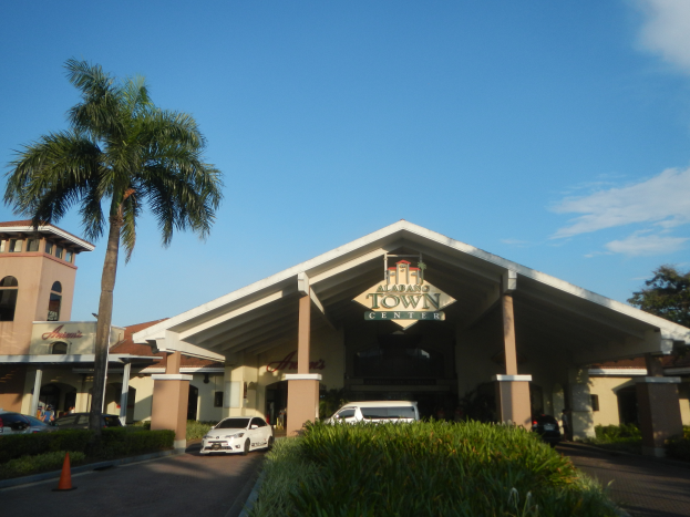 Der Eingang zu einem Resort mit Palmen vorne, umgeben von Gebäuden, Fahrzeugen auf der Straße, Verkehrskegeln, Büschen, Bäumen und einem bewölkten Himmel im Hintergrund.