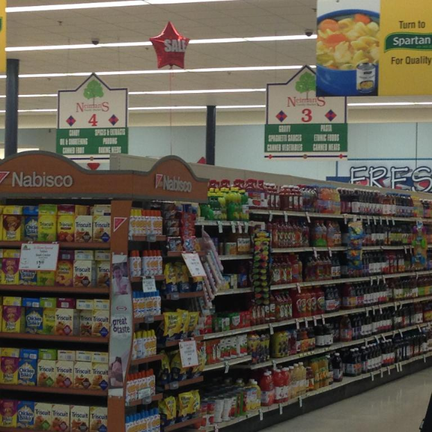 Ein Supermarkt-Innenraum mit sichtbaren Lebensmitteln, Deckenleuchten und hängenden Schildern.