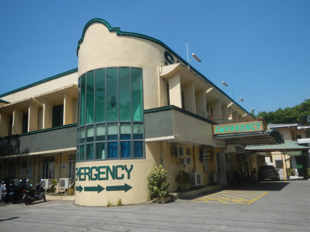 Notfallzeichen an einem Gebäude mit Fahrzeugen, Straßen-Elementen und Grünpflanzen unter einem klaren Himmel.