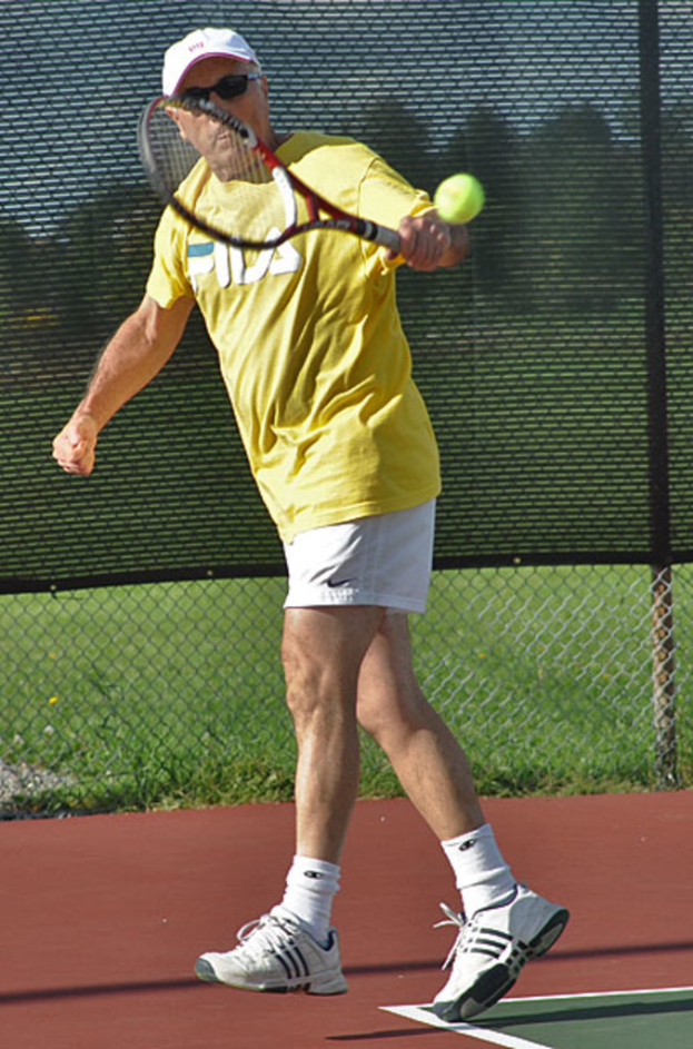 Ein Mann mit Brille, T-Shirt, Kappe und Schuhen spielt Tennis.
