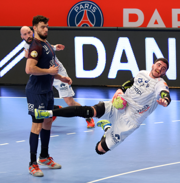 Eine Gruppe von Männern, die Handball auf einem Platz spielen, einer hält einen Ball, mit einem Hintergrund-Schild der Paris Saint-Germain Futsal-Mannschaft.
