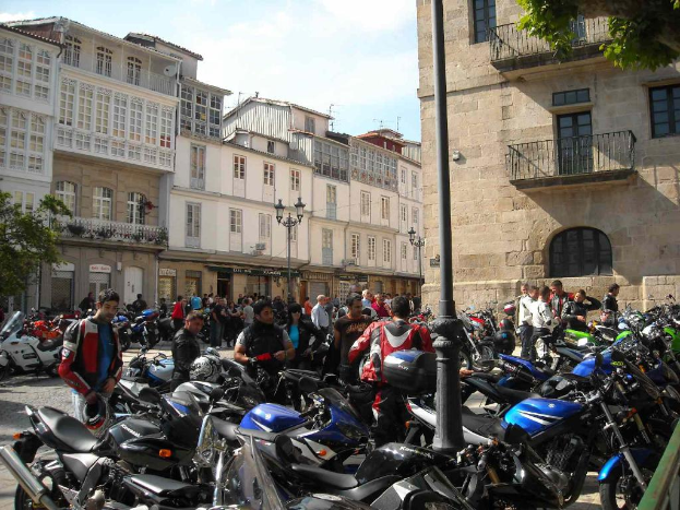 Ein cremefarbenes Gebäude mit zahlreichen Fenstern, das an ein Backsteingebäude mit einer Metallbalustrade angrenzt, mit mehreren abgestellten Fahrrädern und Menschen, die davor diskutieren.