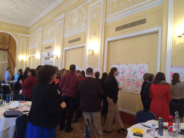 Eine Gruppe von Menschen untersucht Plakate und Charts, die an einer Wand in einem Kunstmuseum zu sehen sind.