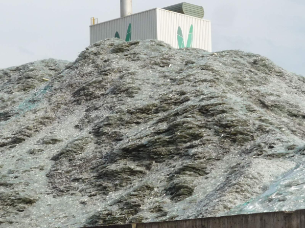 Großer Haufen aus Plastikmüll auf einer Zementwand mit einem Gebäude und einem klaren blauen Himmel im Hintergrund.