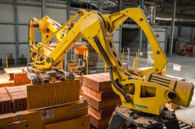 Großes industrielles Lager mit gestapelten Kisten, Kränen, Zaun, Strommasten und einer fernen Wand in einer automatisierten Produktionsumgebung.