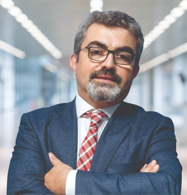 Ein Mann im Anzug und Krawatte mit verschränkten Armen, der eine Brille trägt und vor einem unscharfen Hintergrund steht, beschriftet als der neu ernannte Marketingchef.