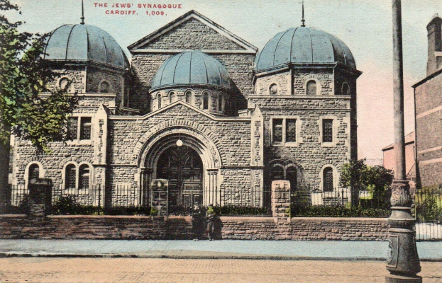 Eine alte Postkarte zeigt die jüdische Synagoge in Cardiff, Ontario, Kanada, mit einem Gebäude mit Fenstern, Türen und Bögen, umgeben von Pflanzen, einem Zaun, Bäumen, einem Pfahl und einem bewölkten Himmel, mit Text oben.
