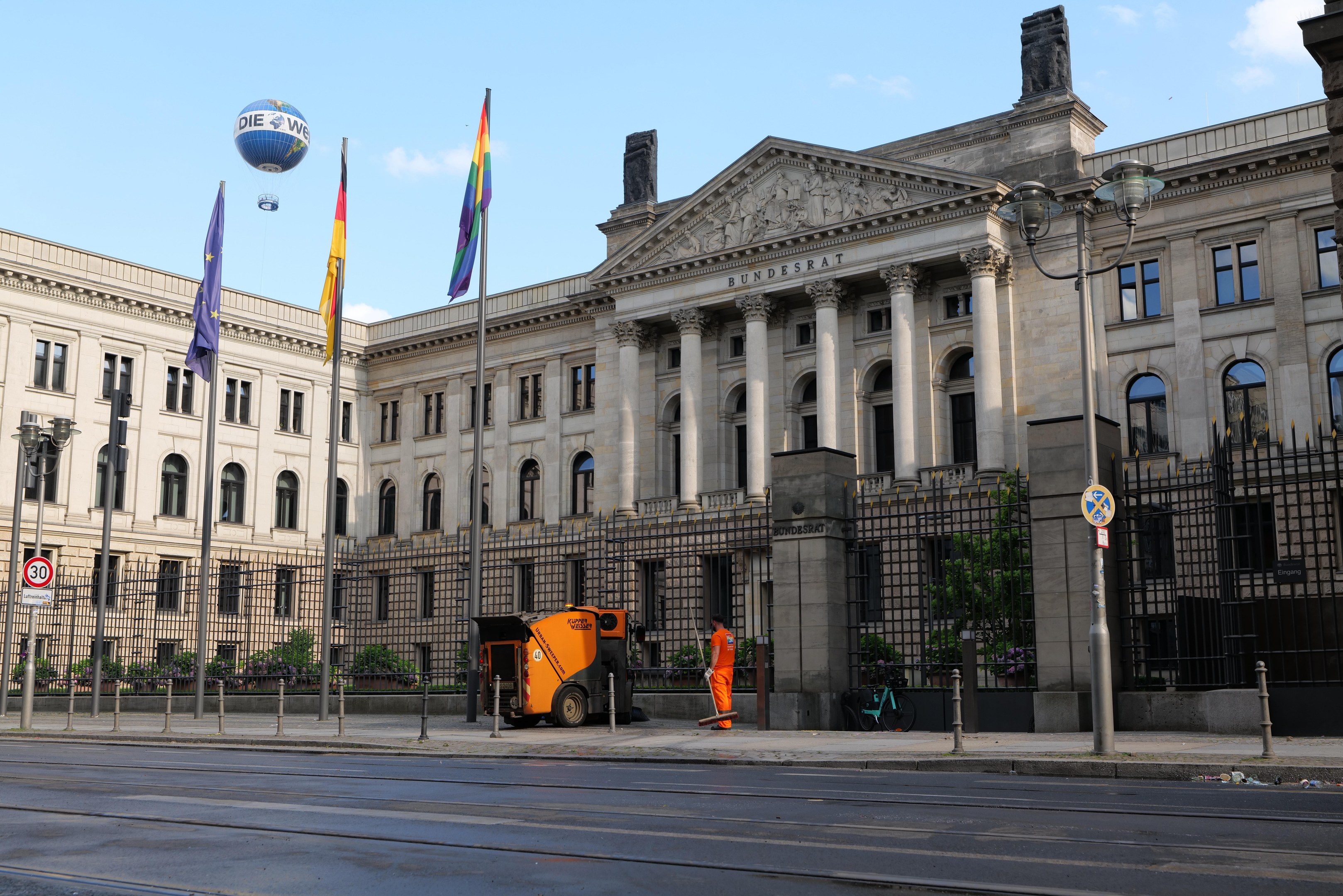 Großes modernes Gebäude mit vielen Fenstern, als Bundestag in Berlin, Deutschland identifiziert, umgeben von Straßeninfrastruktur, Fußgängern und Flaggen, unter einem bewölkten Himmel.