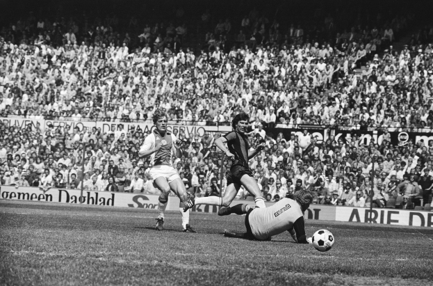 Schwarzes und weißes Foto von Männern, die auf einem Feld Fütbol spielen, mit Zuschauern im Hintergrund und einem Banner "Bundesliga 1978-79 Ajax 1-1 Hannover 96"
