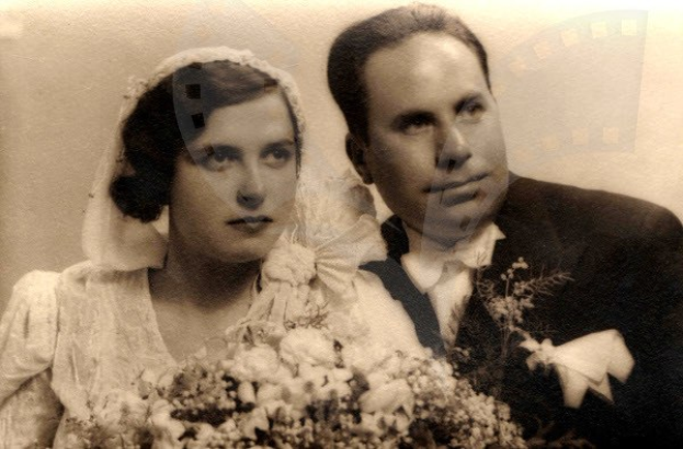 Ein Schwarz-Wei├č-Foto von einem lächelnden Mann und einer Frau, die zusammen auf ihrer Hochzeit stehen, die Frau in einem wei├čem Kleid mit einem Strau├č.