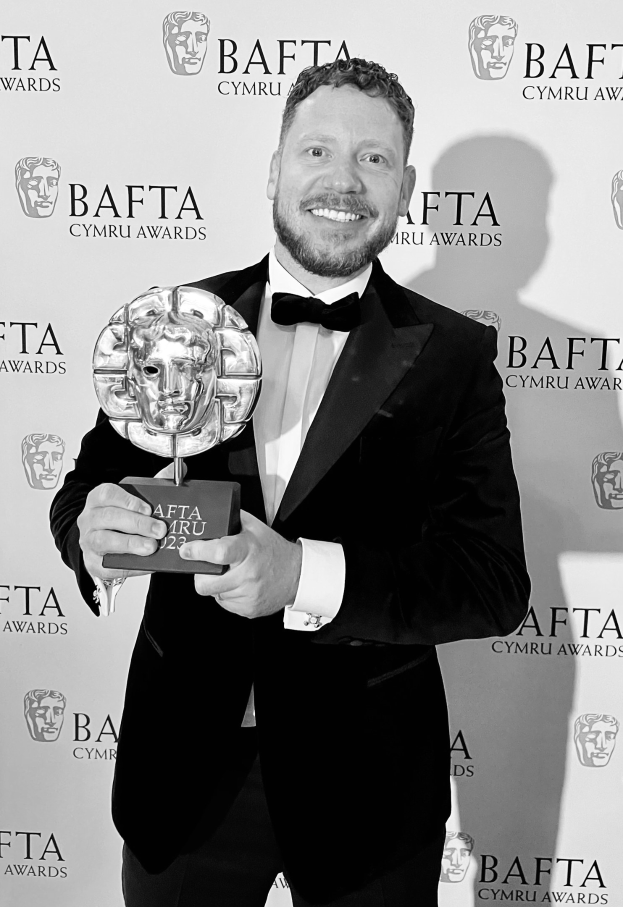 Ein Mann in einem Smoking, der eine BAFTA-Auszeichnung hält und lächelt, mit einem Hintergrundplakat mit der Aufschrift "BAFTA Awards 2018."