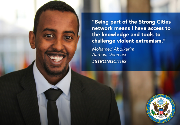 Ein Mann im Anzug und Krawatte, der in die Kamera lächelt, mit einem Logo und Text auf der rechten Seite, der lautet "Teil des Netzwerks starker Städte zu sein, bedeutet, Zugang zu Wissen und Werkzeugen zu haben, um gewalttätigen Extremismus in Frage zu stellen", und einem unscharfen Hintergrund.