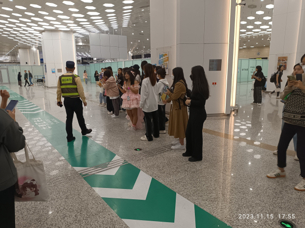 Menschen in der Schlange an einer Flughafen-Sicherheitscheck-Einreichtstelle, mit Taschen und Mobiltelefonen, mit Säulen und Deckenleuchten im Hintergrund.