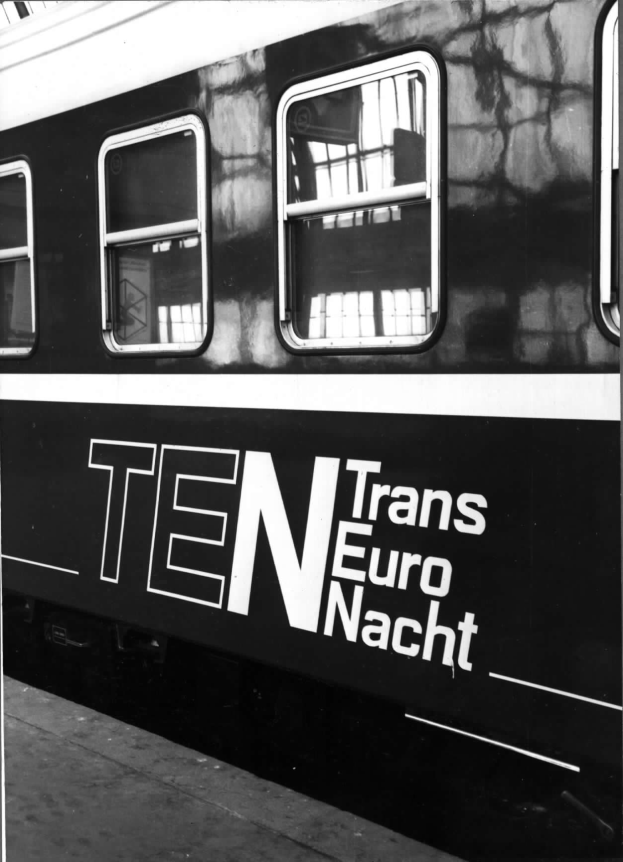 Schwarzes und weißes Foto eines Zuges mit der Aufschrift "Trans Euro Nacht" und Fenstern und einem Bahnsteig unten.