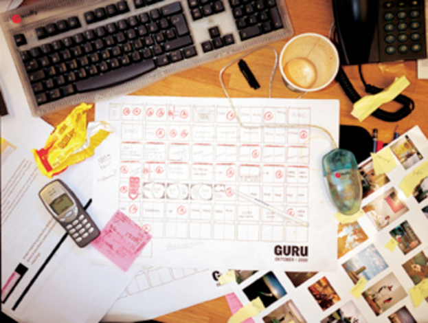 Ein chaotischer Schreibtisch mit Papieren, einem Computer, einem Telefon, Tassen und einem mobile Phone.