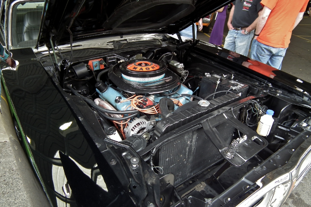 Ein Nahaufnahme von Autokühlerteilen mit unscharfen Personen und einer Straße im Hintergrund.