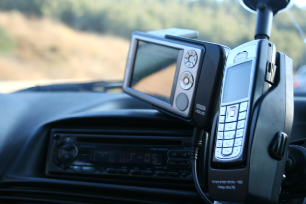 Ein Telefon auf einem Mobilständer mit einer Kamera, Kabel und MP3-Player auf der linken Seite, ein Glas und unscharfe Gegenstände im Hintergrund.