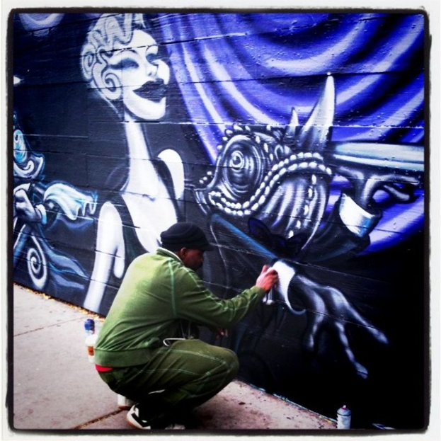 Eine Person mit einer Flasche in der Hand und mehreren anderen Flaschen auf der Straße sowie einer mit Graffiti bedeckten Wand im Hintergrund.