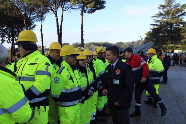 Eine Gruppe von Menschen in gelben Westen und Helmen, einige mit Mützen, die zusammen auf einer von Bäumen umgebenen Straße unter einem klaren blauen Himmel stehen.