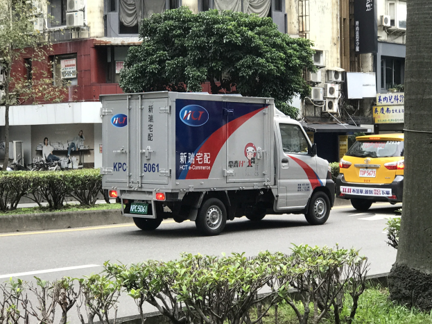 Ambulanz auf der Straßenseite neben einem Baum geparkt mit Fahrzeugen, Gebäuden und anderen Objekten im Hintergrund.