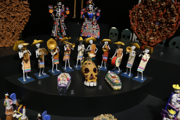 Tag der Toten Ausstellung im Fine Arts Museum in San Francisco, mit Spielzeugen, Schädeln und anderen Gegenständen auf einer schwarzen Oberfläche mit einer dekorierten Wand im Hintergrund.