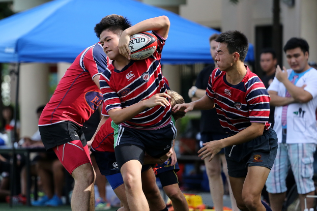 Eine Gruppe von Menschen, die draußen ein Spiel spielen, während ein Junge in der Mitte einen Ball hält und andere im Hintergrund stehen und zuschauen.