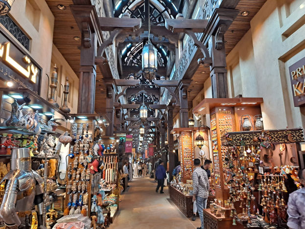 Ein geschäftiges Dubai-Markt mit Menschen, die zwischen Regalen voller Gegenstände hindurchgehen, Wänden mit Text und einer Decke mit warmem Licht.