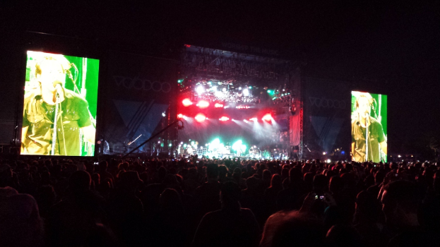 Eine Konzertszene mit einer Menge unten, einem großen Bildschirm links und einem weiteren Bildschirm rechts.