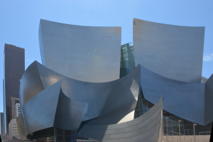 Das ARTIST Concert Hall in Los Angeles, ein modernes Gebäude mit Glaswänden und Treppen mit Geländern, die zum Eingang führen, mit Menschen, die herumgehen und anderen Gebäuden im Hintergrund unter einem klaren blauen Himmel.
