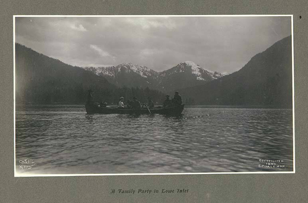 Schwarze und weiße Fotografie einer Familie in einem Kanu auf einem See mit Bergen und Bäumen im Hintergrund, Himmel oben sichtbar und Text unten.
