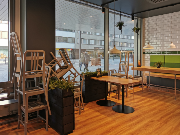 Ein Berliner Restaurant mit Holztischen und -stühlen vor einem großen Fenster, das auf eine Straße mit Fußgängern, Gebäuden und städtischen Elementen blickt.