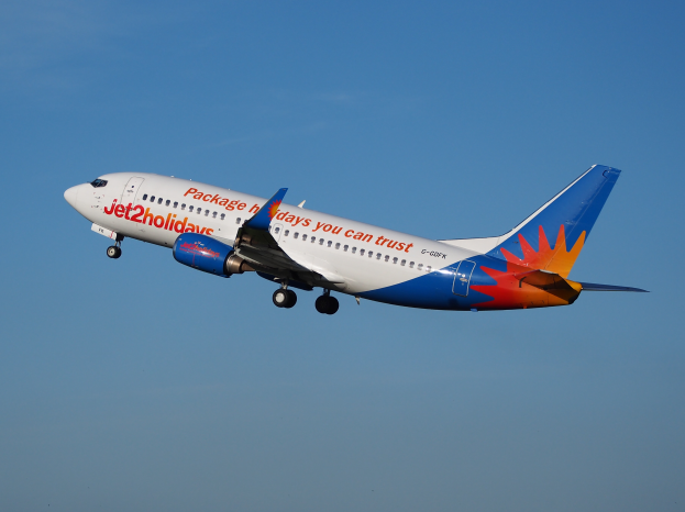Ein Jet2holidays Airbus A320-200-Flugzeug im Flug mit einer weißen, blauen, orangen und roten Lackierung gegen einen blauen Himmel.
