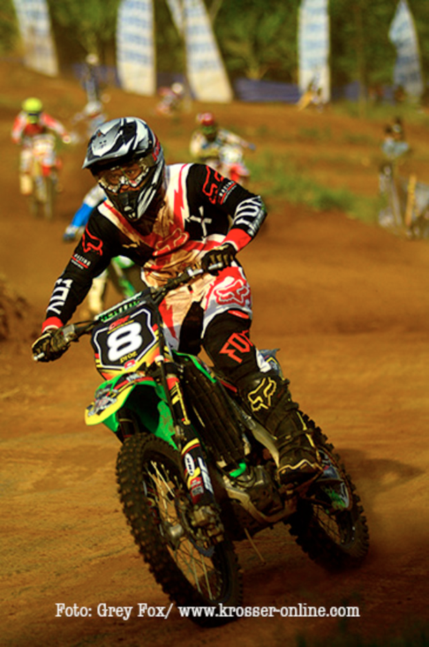 Mehrere Personen auf Motorrädern bei einem Rennen, alle mit Helmen, mit Text am unteren Bildrand.