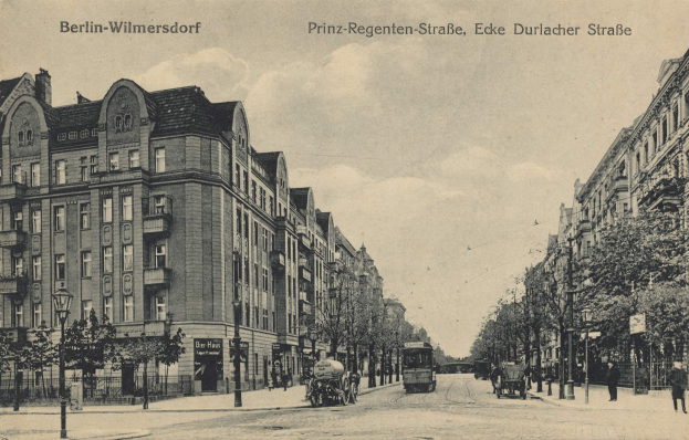 Ein altes Schwarz-Weiß-Foto einer Stadtstraße in Berlin-Wilmersdorf, das Gebäude, Bäume, Straßenlaternen, Straßenlaternen, Kraftfahrzeuge, Fußgänger und einen bewölkten Himmel zeigt, mit der Aufschrift "Berlin-Wilmersdorf - Prinz Regenten-Straße, Eke Durlacher Straße" oben.