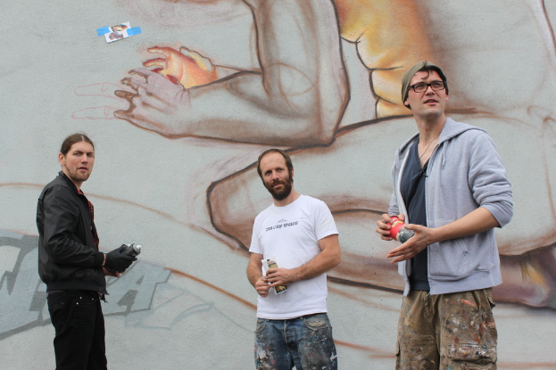 Menschen stehen und halten Farbsprühflaschen vor einer graffiti-bedeckten Wand.