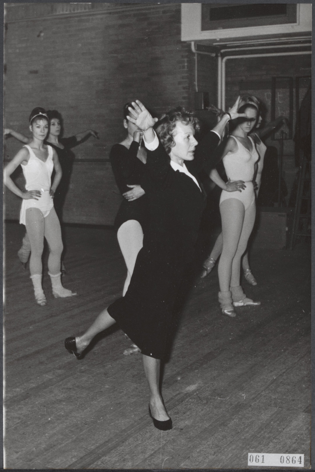 Eine Gruppe von Frauen, die in einem Schwarz-Weiß-Foto tanzen, wobei die zentrale Frau Tanzschuhe trägt, in einem Studio mit einer Wand im Hintergrund.