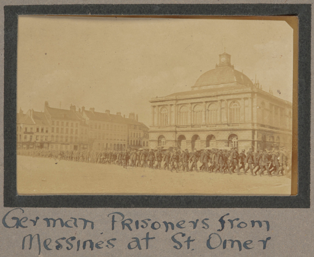 Gruppe deutscher Gefangener aus Messines vor einem Gebäude mit einem klaren blauen Himmel im Hintergrund, lesbarer Text unten.