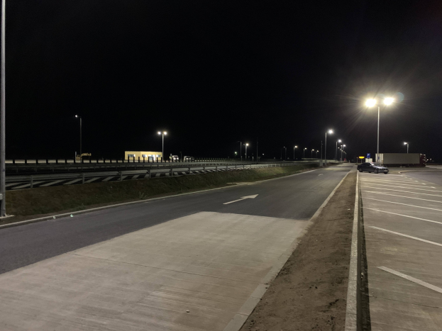 Auto auf einer Autobahn bei Nacht mit Straßenlaternen, die die Szene beleuchten, grasbewachsenen Umgebungen und einem sichtbaren Himmel im Hintergrund.