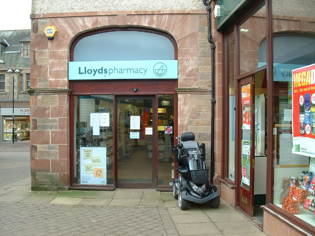 Eine Apotheken-Filiale mit einem vor dem Gebäude geparkten Auto und einem Gebäude auf der linken Seite.