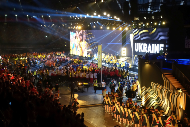 Eine große Menschenmenge auf einer hell erleuchteten Bühne mit Musikern und einem Bildschirm im Hintergrund, was auf ein Ereignis in Zusammenhang mit der Ukraine hindeutet.