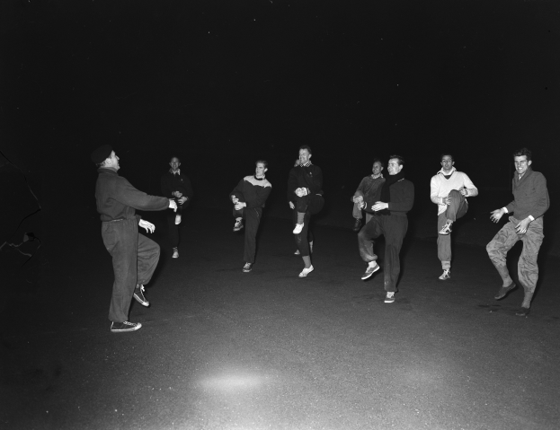 Eine Gruppe von Männern auf einer Bühne in einer Schwarz-Weiß-Einstellung, die Schuhe tragen, wahrscheinlich während einer Vorstellung.