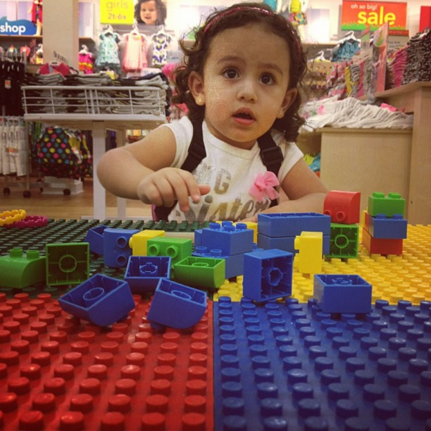 Ein Baby spielt mit bunten Blöcken, während andere Kinder im Hintergrund zu sehen sind.