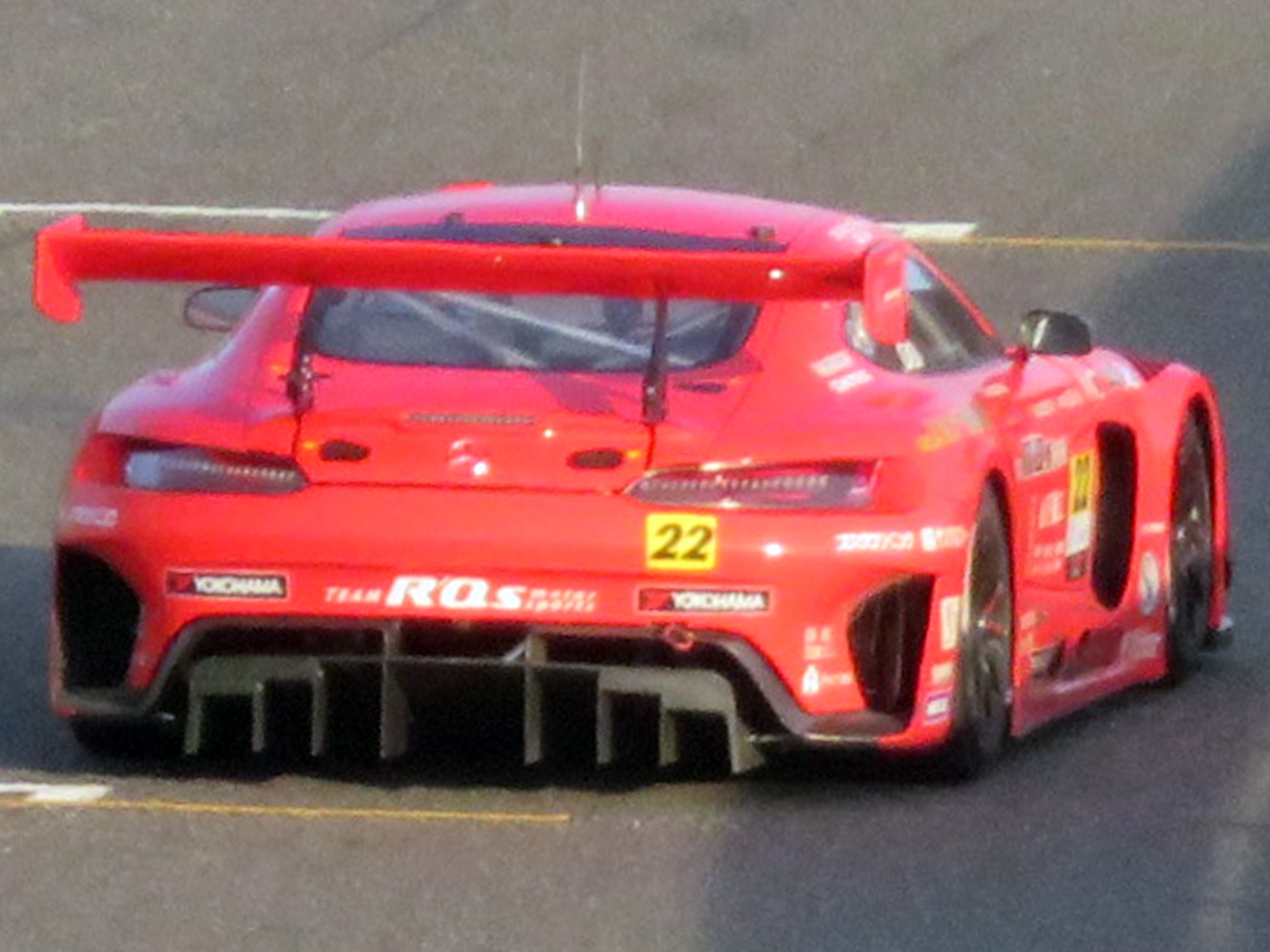 Roter Porsche 911 GTS Rennwagen auf einer Rennstrecke mit aerodynamischem Design, großem Heckflügel und schwarzen Rädern.