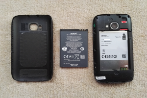 Ein Nokia Asha 501 Mobiltelefon mit entfernter Batterie und Rückseite, das auf einer cremefarbenen Oberfläche liegt.