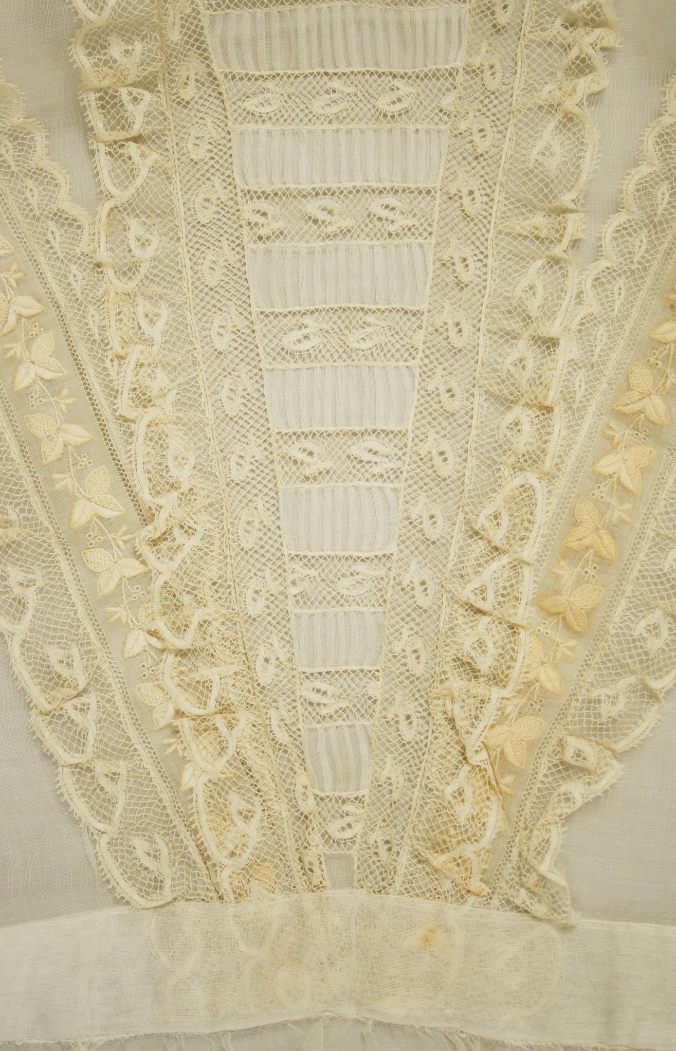 Nahaufnahme eines weißen Kleides mit zarter, detailreicher Spitze in verschiedenen Formen und Mustern auf leichtem, luftigem Stoff.