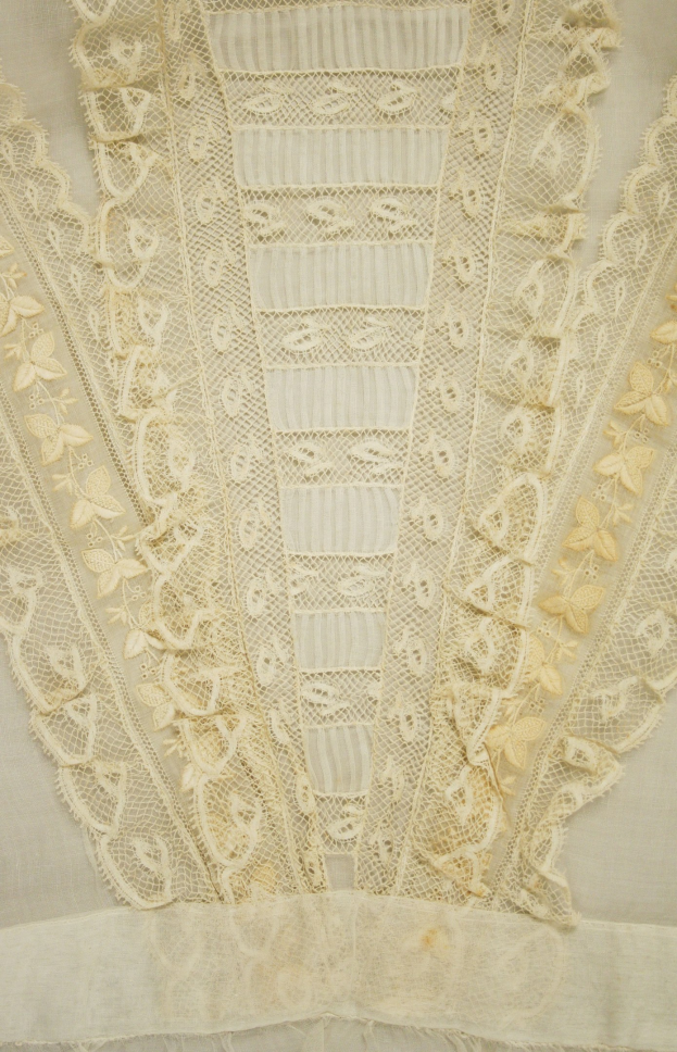 Nahaufnahme eines weißen Kleides mit zarter, detailreicher Spitze in verschiedenen Formen und Mustern auf leichtem, luftigem Stoff.