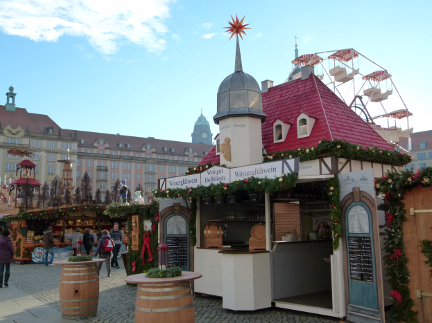 Ein geschäftiger Weihnachtsmarkt in Nürnberg, Deutschland, mit Menschen um geschmückte Stände, festliche Lichter, einem Riesenrad im Hintergrund und einer Schautafel rechts.